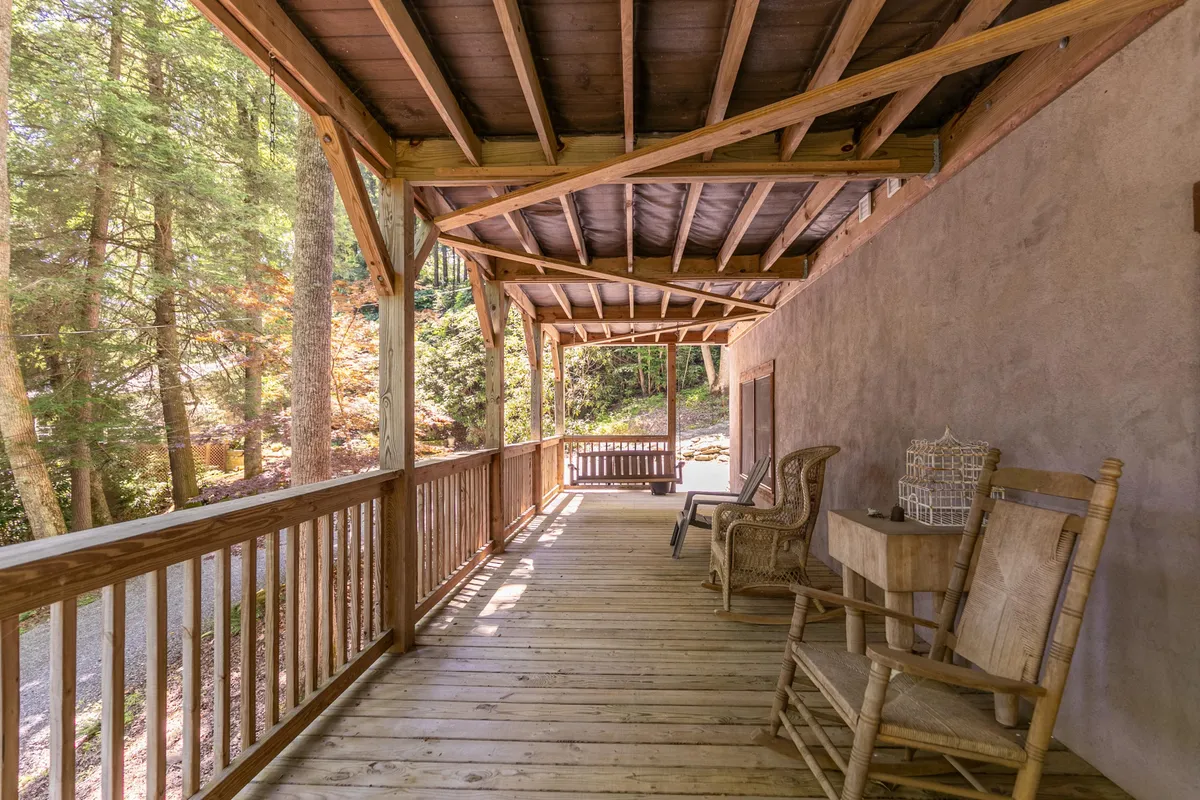 A wooden porch with classic rocking chairs and a table, embraced by lush trees and serene forest ambiance. The calm setting highlights the tranquility and closeness to nature that guests can experience while staying at Bucks Cabin.