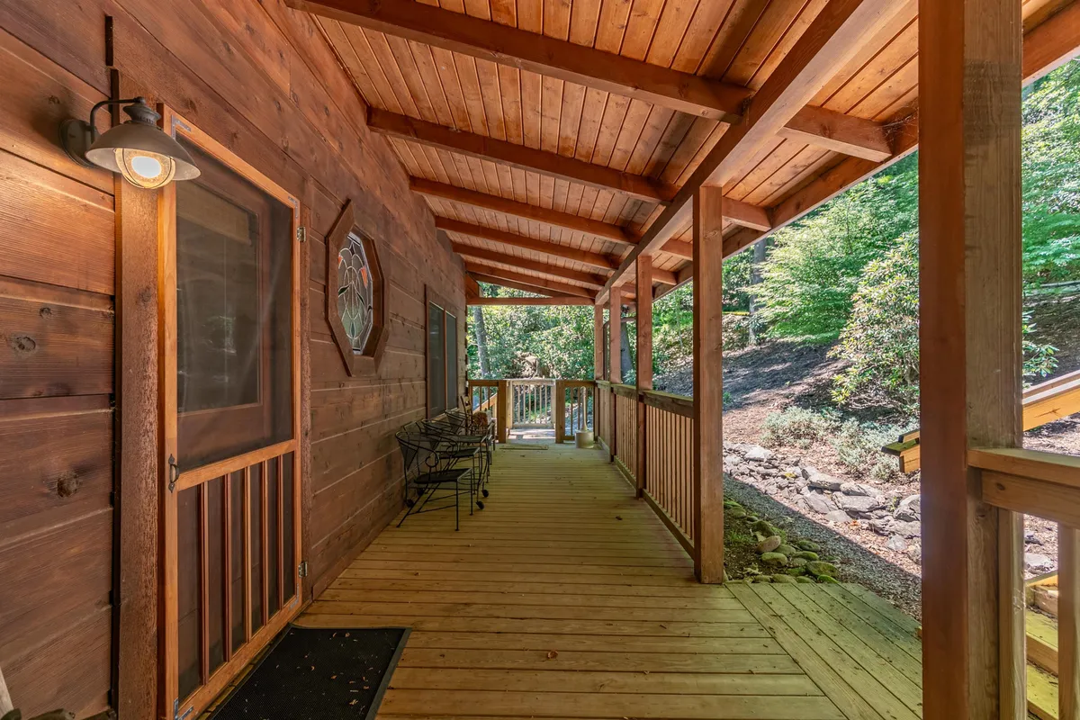 A relaxed exterior porch scene featuring wooden beams, a deck railing, comfortable seating, and expansive views of the natural surroundings. The porch invites guests to unwind after outdoor excursions, with hints of sunrise or sunset lighting.