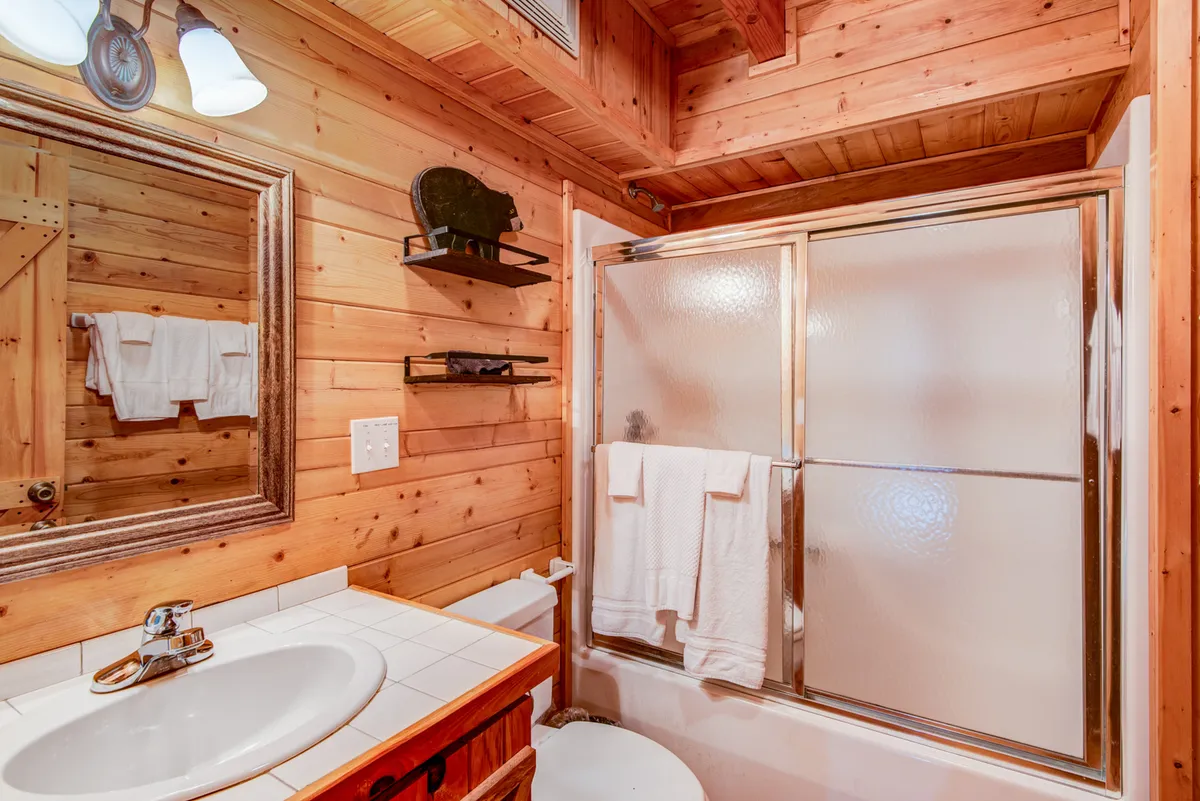 A warm, inviting bathroom with wooden walls, a mirror, a sink, and a shower area. The space suggests both function and relaxation, supporting guests' self-care routines and daily comfort.