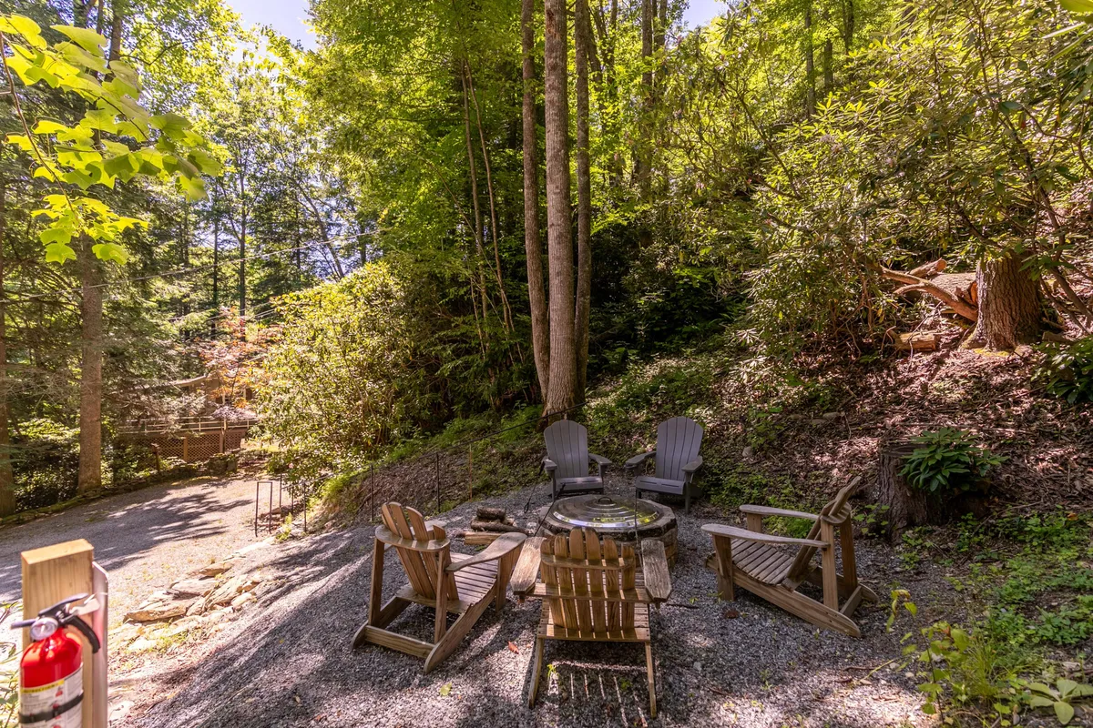 This exterior image features a cozy fire pit surrounded by wooden chairs amidst lush greenery, evoking the classic campfire gathering atmosphere. The setup is ideal for groups to enjoy late-night storytelling, laughter, and star-gazing under the open sky.