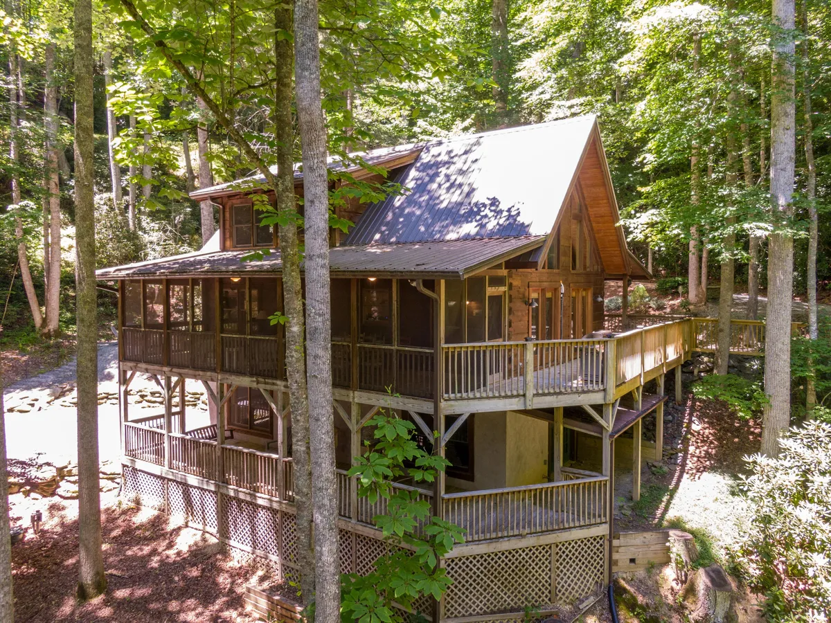 The wooden deck and screened porch are front and center in this image, set against a backdrop of mature trees. The scene radiates a relaxed, inviting energy, perfect for outdoor dining or simply soaking in the sights and sounds of nature from the comfort of a protected space.