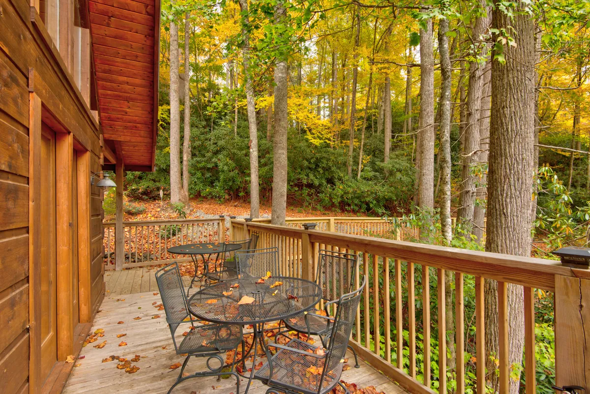 An inviting wooden deck is set in the midst of fall foliage, with a dining table and chairs perfect for shared meals or outdoor games. The deck is surrounded by trees, providing privacy and a deep sense of connection to nature.