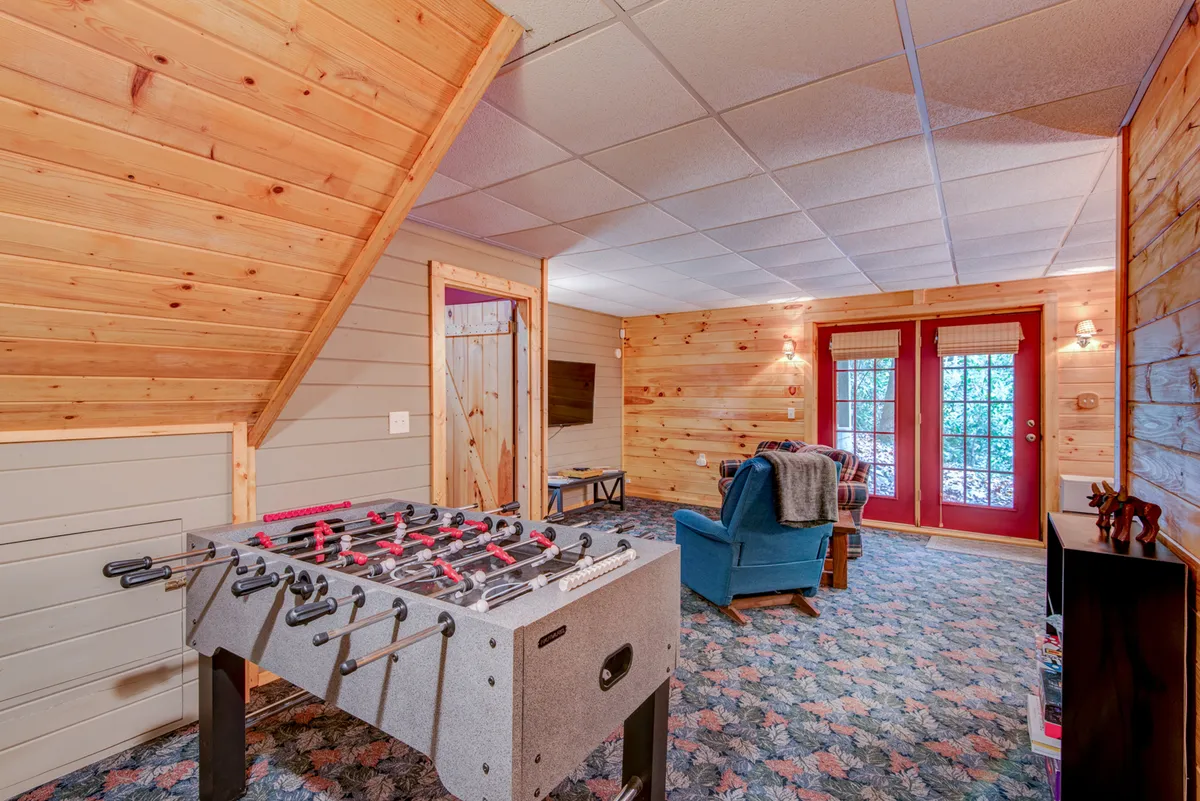 Featuring a foosball table, comfortable blue armchair, and double doors leading outside, this space blends playful indoor activities with a visual link to the outdoors. The setup suggests a seamless flow from playtime to relaxation and highlights the den’s direct access to the porch.