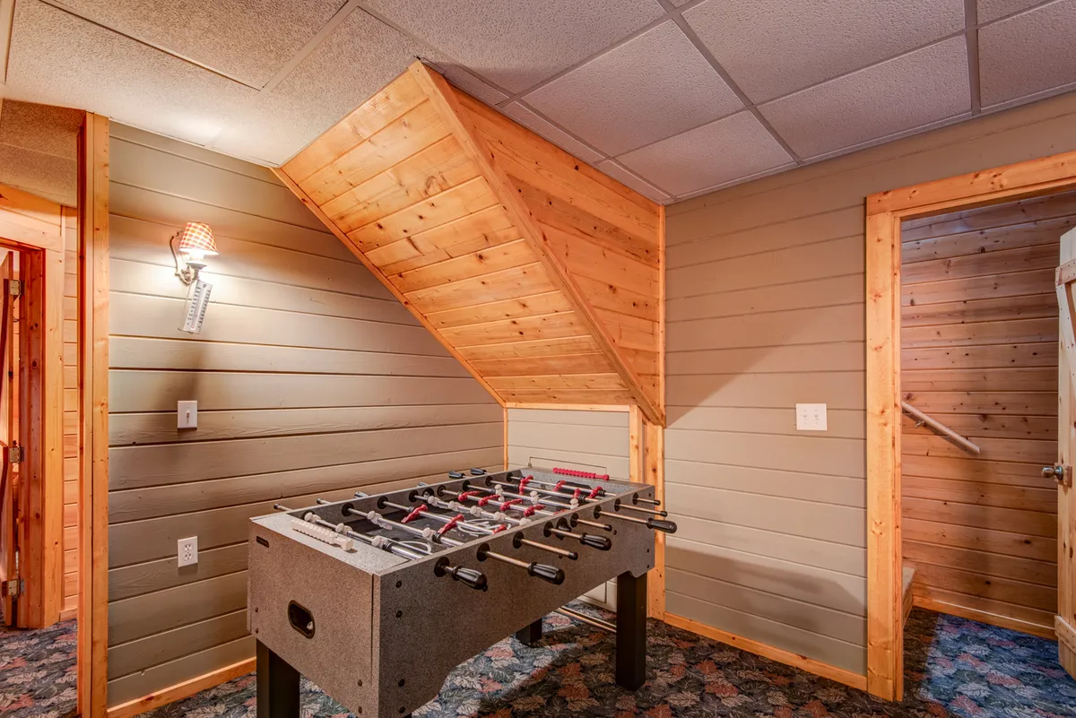 This image reveals an interior den with a foosball table and rustic wooden paneling, creating a playful, family-friendly atmosphere. Doorways lead to other parts of the home, suggesting the multi-level layout mentioned in the text.