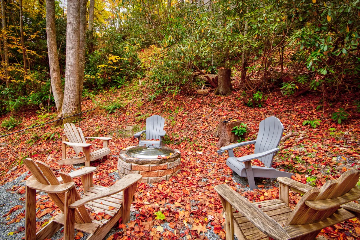 The photo showcases a cozy fire pit area ringed with Adirondack chairs and surrounded by vibrant fall foliage. The scene evokes gatherings, storytelling, and evenings spent stargazing or sharing family memories after a day of exploration.