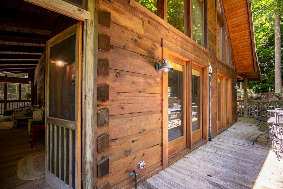 A welcoming exterior view of the cabin featuring a spacious screened porch and deck, surrounded by beautiful greenery. The space invites guests to enjoy outdoor dining, quiet mornings with coffee, or simply relax while immersed in nature.